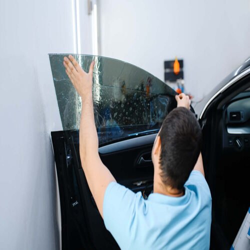 Male worker tries on sheet of car tinting, tuning service. Mechanic applying vinyl tint on vehicle window in garage, tinted automobile glass